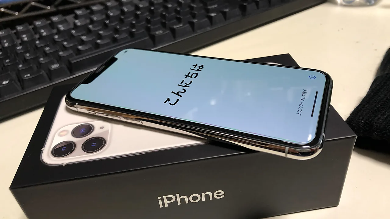 iPhone 11 Pro warna Silver tergeletak miring di atas kotak kemasan iPhone, layar menyala menampilkan sapaan awal penyiapan