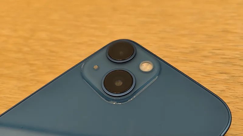 Modul kamera ganda diagonal pada punggung iPhone 13 warna biru di atas meja kayu