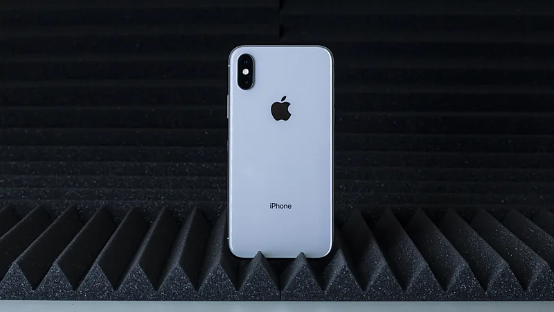 Punggung iPhone XS warna perak dengan dua kamera tersusun vertikal di sudut kiri atas, berdiri di atas peredam suara hitam
