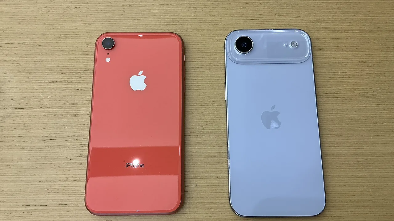 Punggung iPhone XR warna coral di sebelah kiri, berdampingan dengan iPhone keluaran baru berwarna putih, keduanya tergeletak di meja kayu