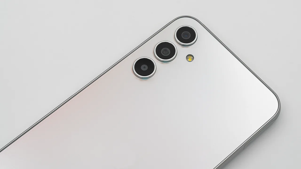 Sudut atas punggung Samsung Galaxy A34 5G warna perak di atas latar putih, memperlihatkan tiga lensa kamera melingkar dan lampu kilat kuning