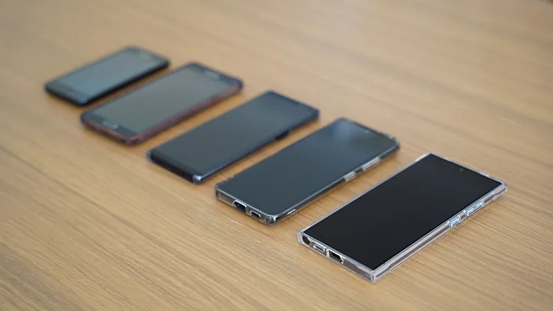 Lima HP Samsung berbagai generasi dijejer dari yang paling kecil ke paling besar di atas meja kayu, semuanya dalam keadaan layar mati